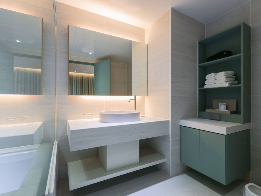 Un baño moderno con ducha de vidrio, lavamanos blanco con un espejo grande y un mueble de tocador verde con estantes.