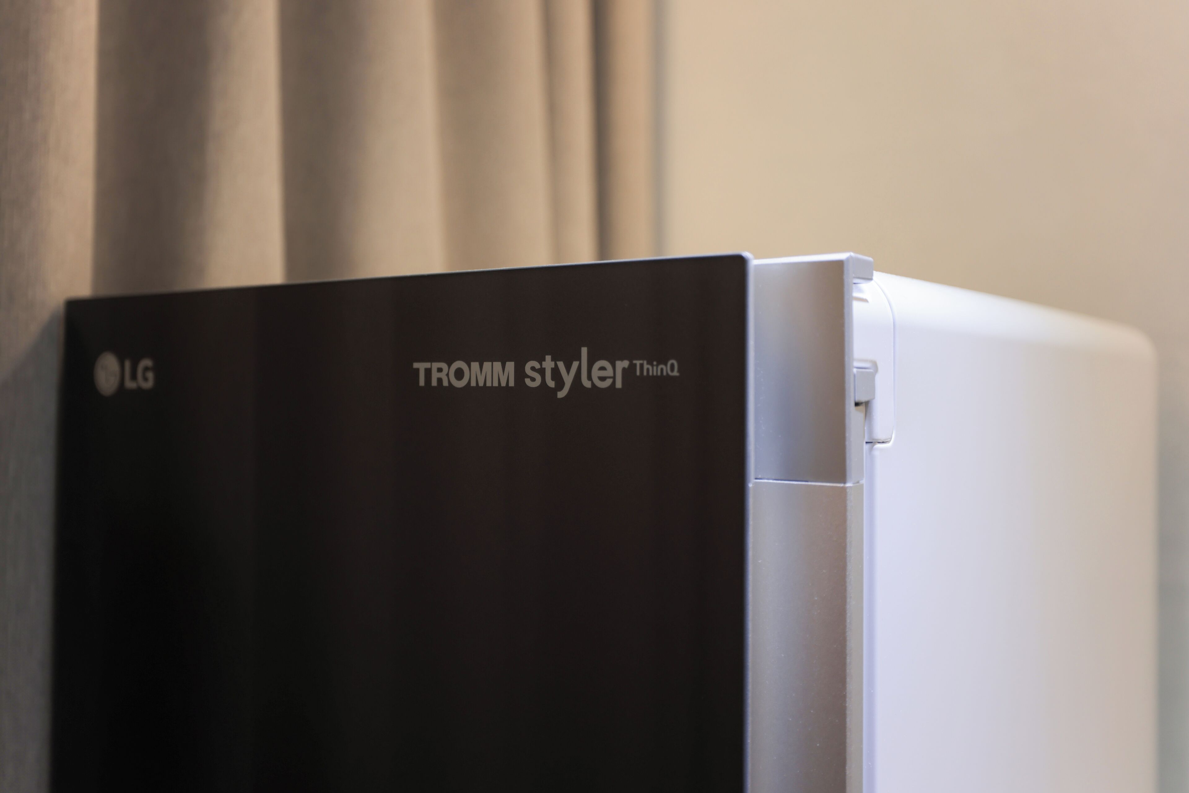 A black LG refrigerator with a white side panel, placed against a wall with a curtain.