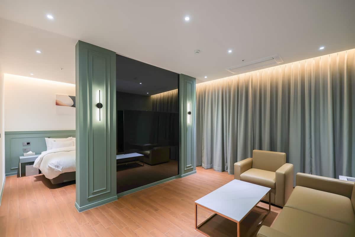 A modern hotel room with a bed, a seating area with a table, a large mirror, and a view of a curtain-covered window.