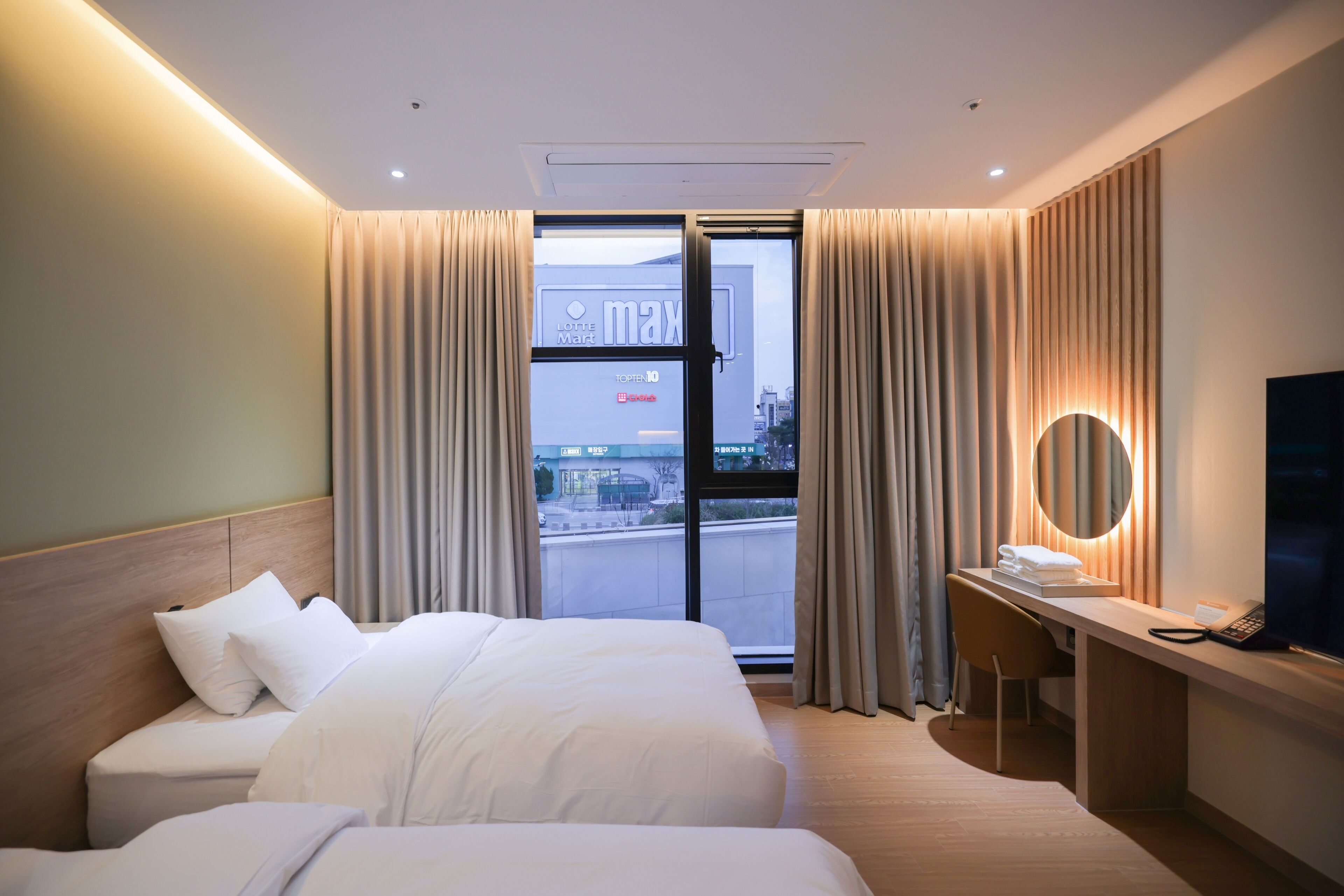 A hotel room with a bed, a desk, a chair, a TV, and a view of the outside.