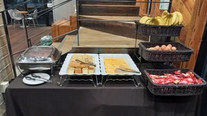 Una mesa de buffet con diversos alimentos y utensilios, ubicada en una sala con una escalera y vistas al exterior.
