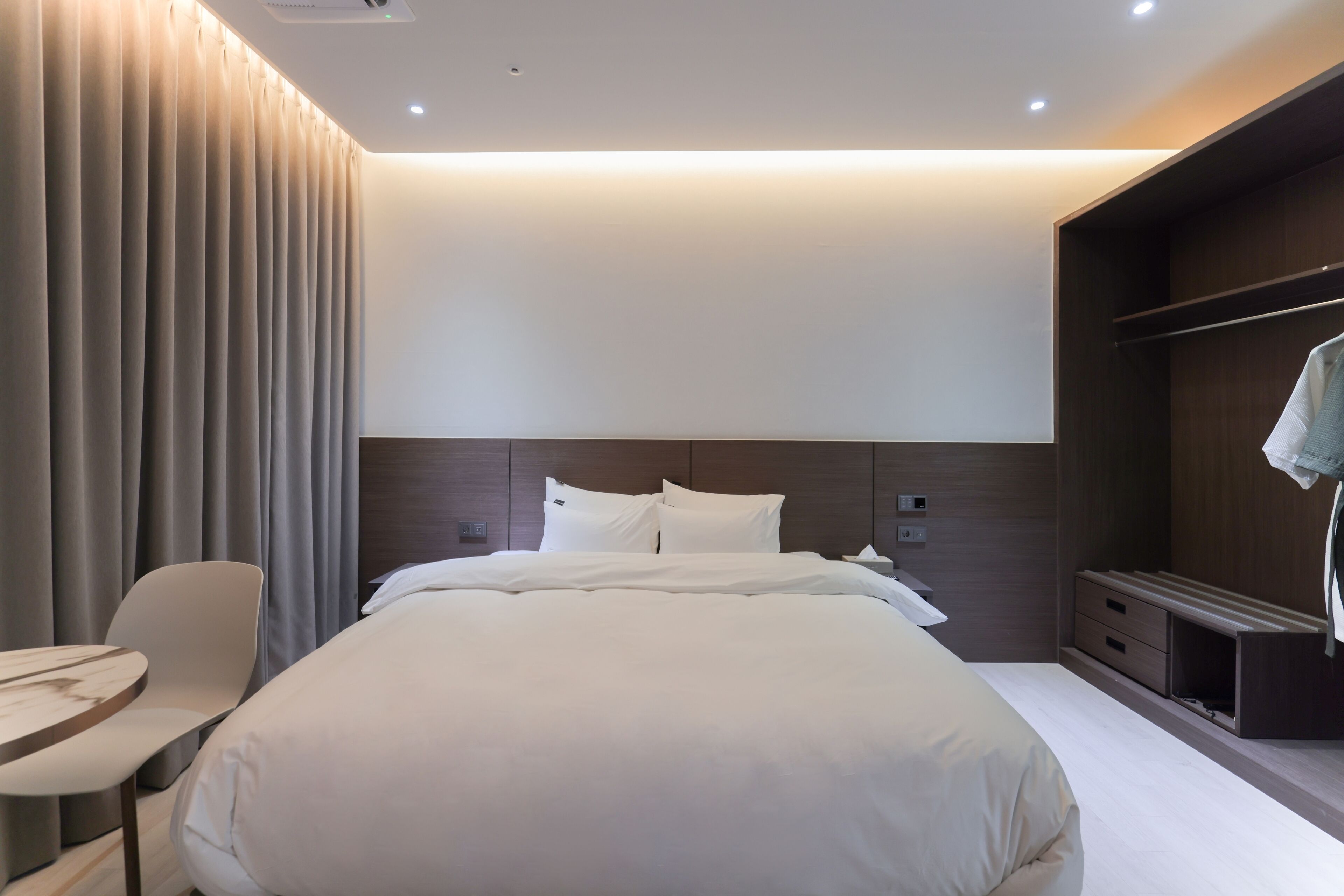 A modern hotel room with a large bed, a desk, and a wardrobe.
