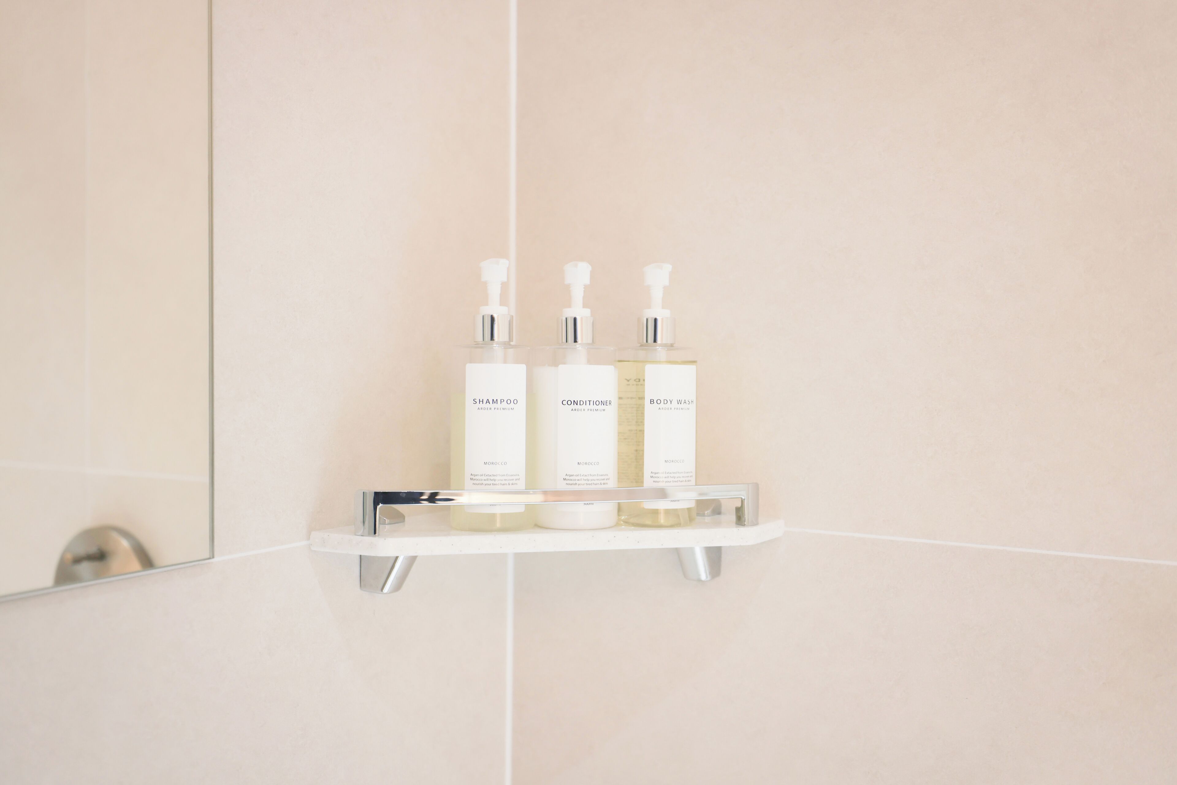 Un baño con un estante blanco que contiene tres botellas de champú, acondicionador y gel de ducha.