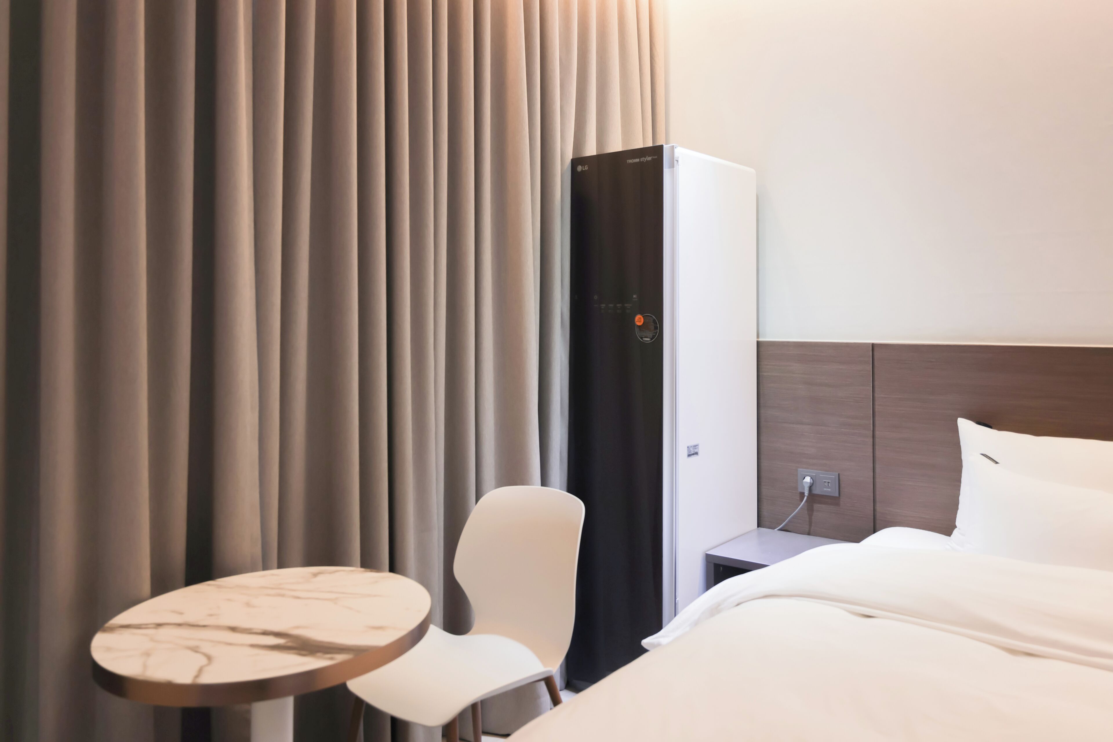 A hotel room with a bed, a table, a chair, and a minibar.