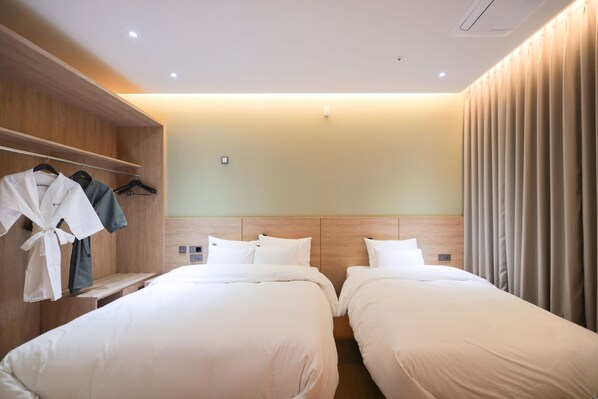 A hotel room with two beds, a wooden wardrobe, and a robe rack.