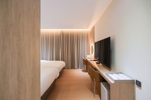 Ein modernes Hotelzimmer mit Bett, Schreibtisch mit Stuhl, Fernseher und einem großen Fenster mit Vorhängen.