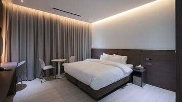 A modern hotel room with a large bed, bedside table, and a small desk with a chair.