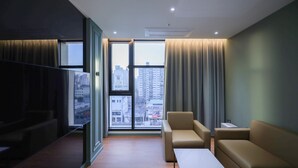 Habitación de hotel moderna con un ventanal grande, un sofá, una mesita y un televisor de pantalla plana.