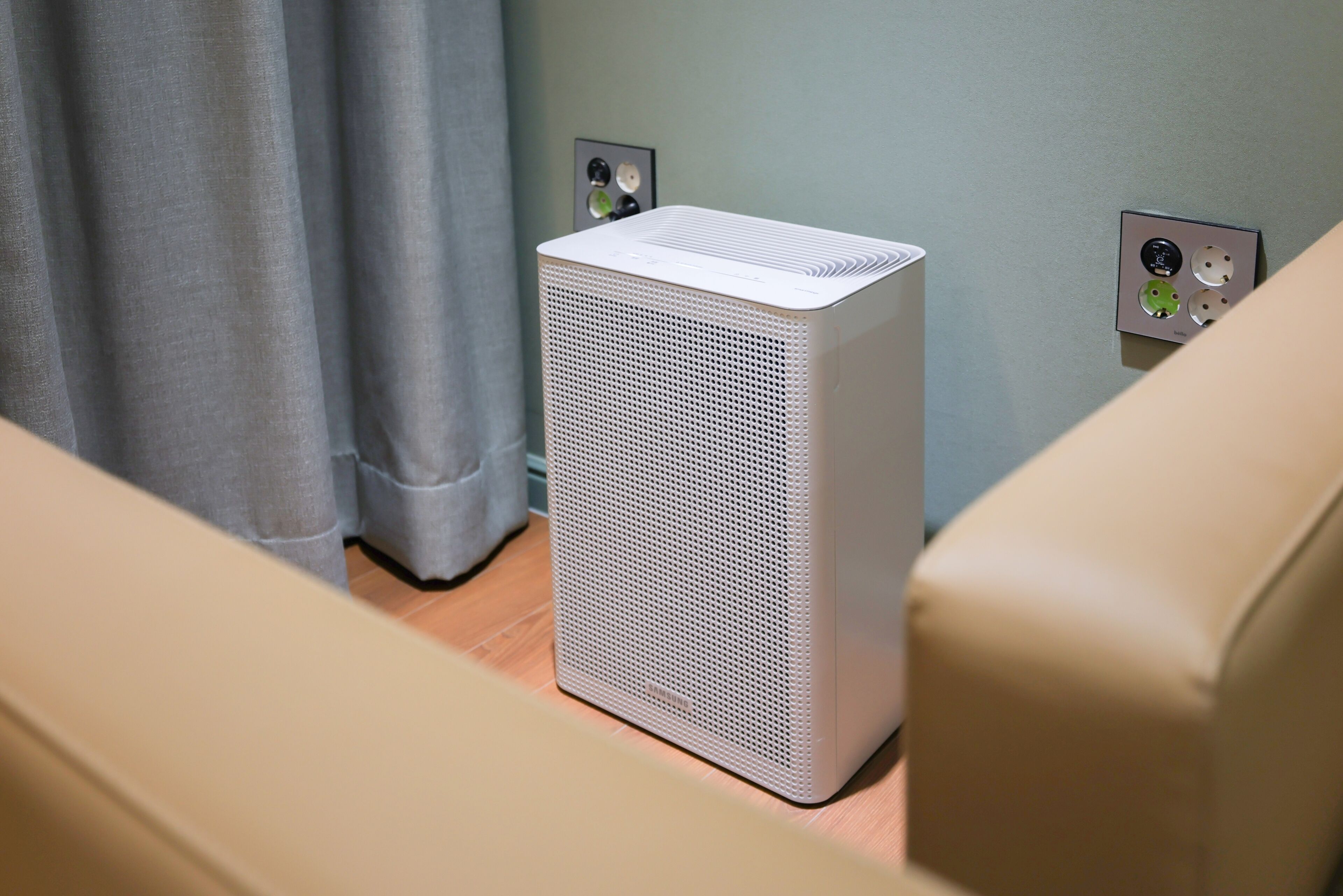 A white portable air conditioner in a room with a light-colored sofa and a curtain.