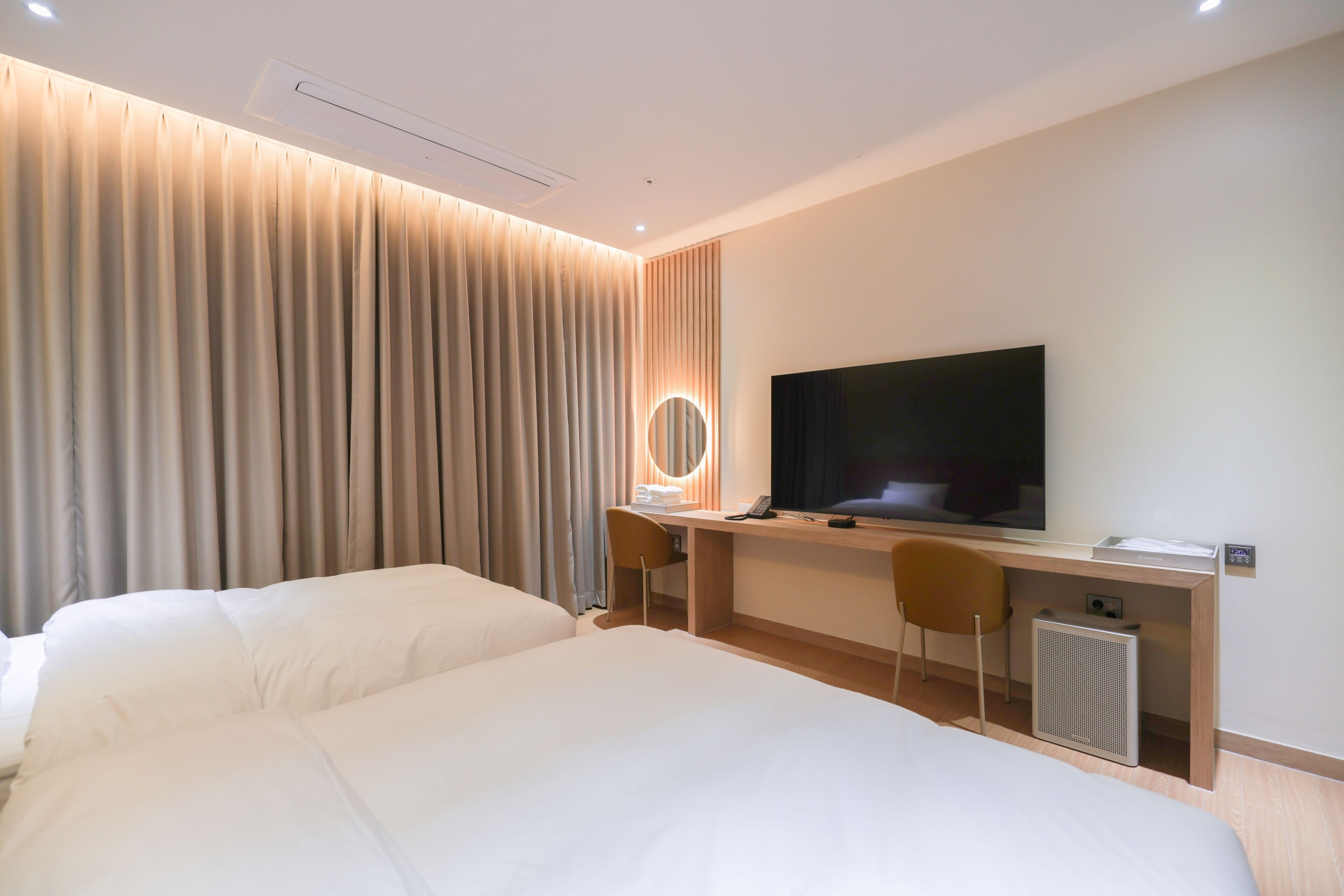 Ein Hotelzimmer mit zwei Betten, einem Schreibtisch, einem Computer, einem Fernseher und einem Spiegel.