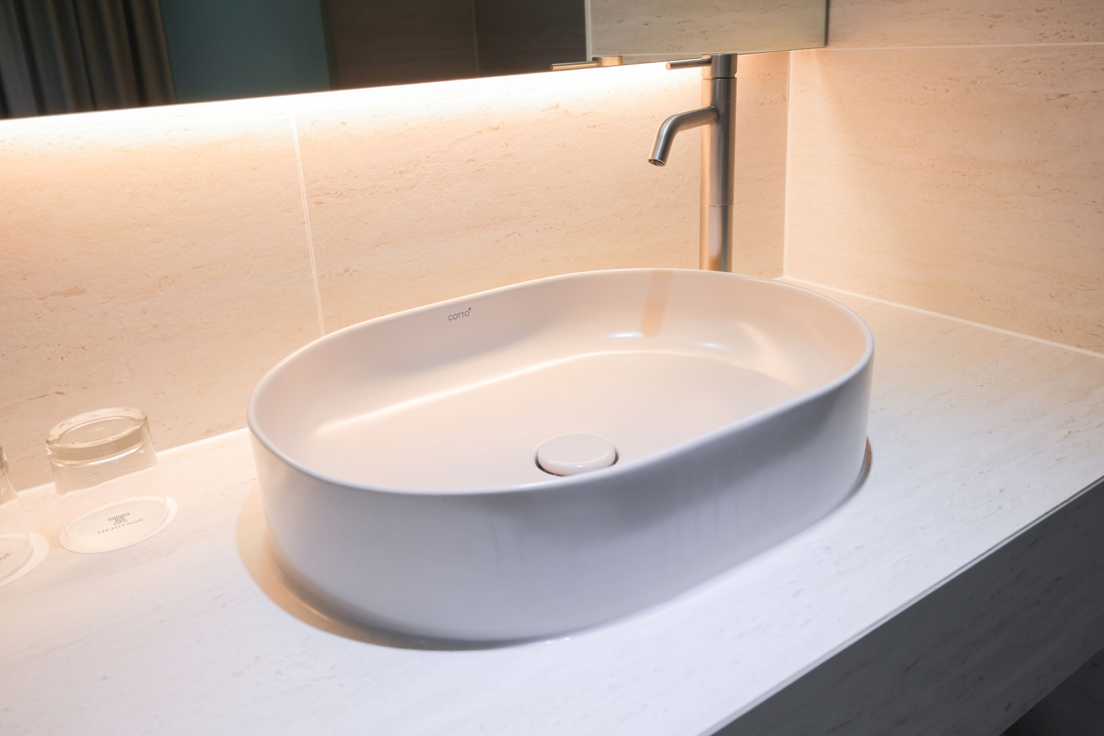 Un baño moderno con un lavamanos de cerámica blanca, un espejo encima y pared con azulejos.