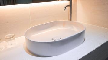 Un baño moderno con un lavamanos de cerámica blanca, un espejo encima y pared con azulejos.