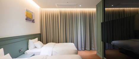 A hotel room with two beds, a large window with curtains, a wall-mounted air conditioner, and a painting.