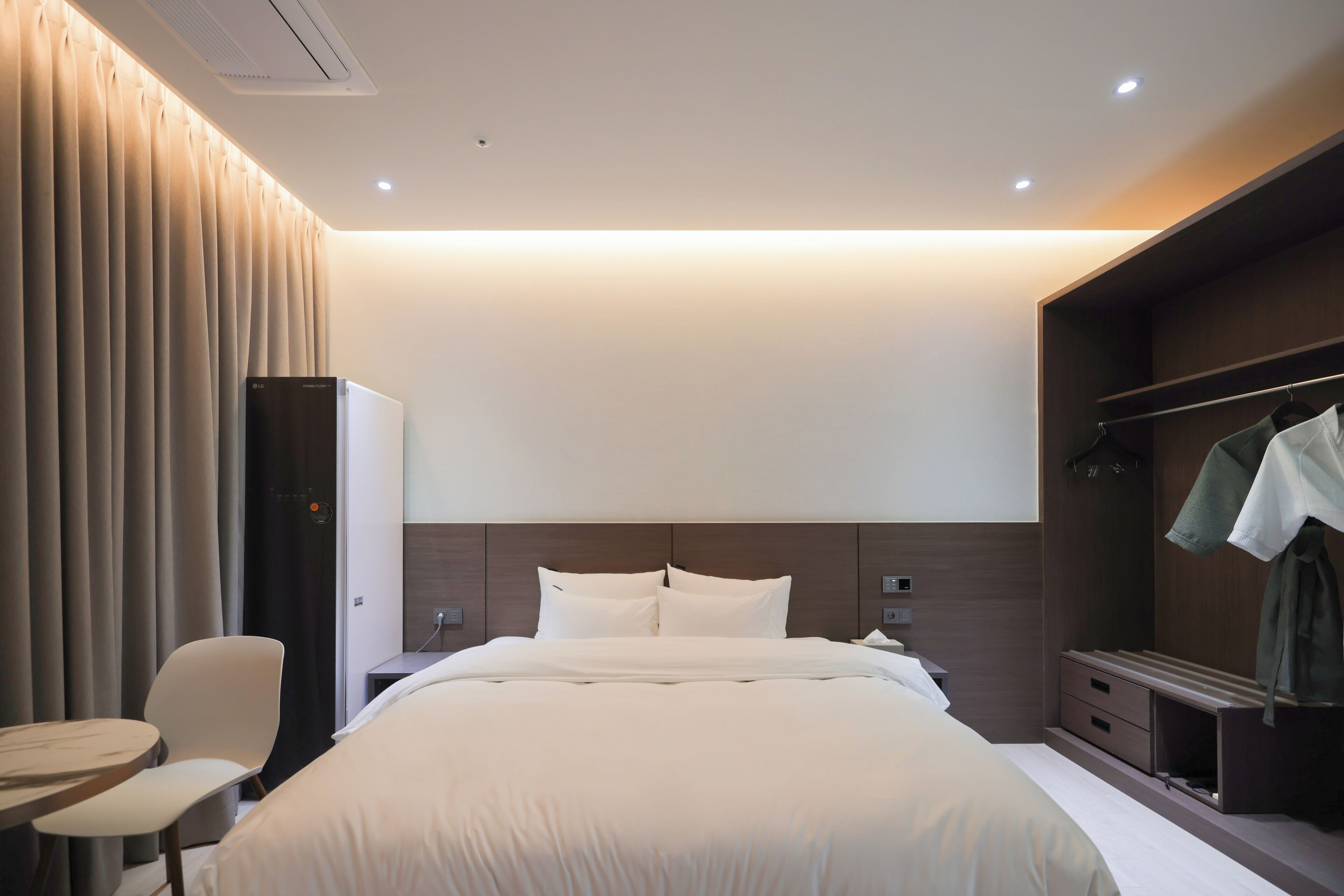 A modern hotel room with a large bed, a desk, a chair, and a wardrobe.