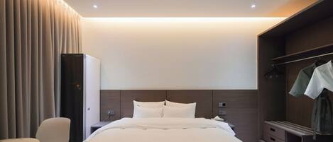 A modern hotel room with a large bed, a desk, a chair, and a wardrobe.