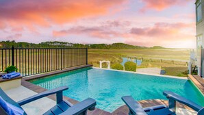 Une piscine avec des chaises longues, une vue sur une zone marécageuse et un ciel au coucher du soleil.
