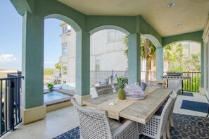 A covered outdoor dining area with a pool, wicker furniture, and a grill.