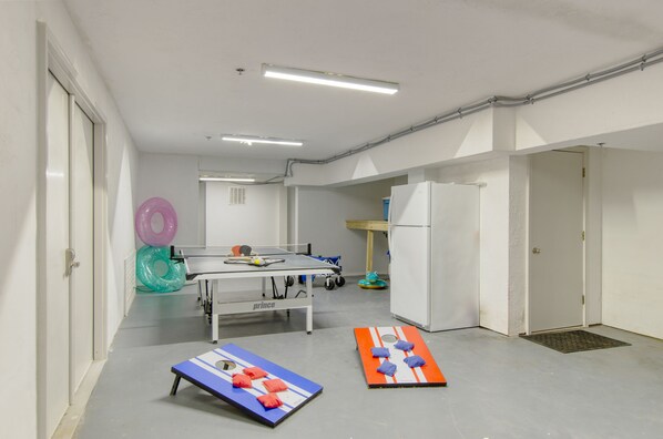 A room with a ping pong table, two exercise mats, and a refrigerator.