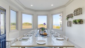 Une salle à manger avec une longue table dressée pour le repas, de grandes fenêtres donnant sur la plage et des œuvres d’art décoratives accrochées aux murs.