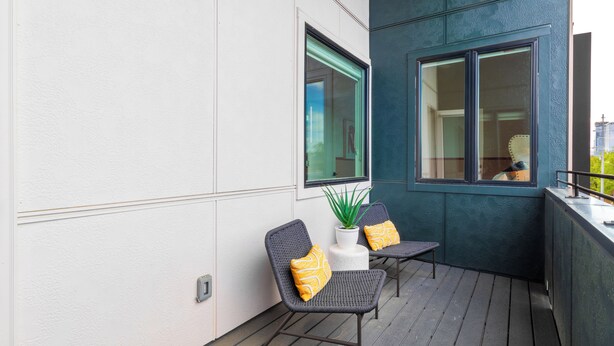 Ein Balkon mit zwei Stühlen, einem Blumentopf und einem Fenster mit Blick auf die Stadt.