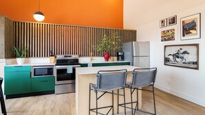 Eine moderne Küche mit grünen Schränken, einer Wand aus Holzlamellen, einer zentralen Kochinsel mit Barhocker und verschiedenen Küchengeräten.