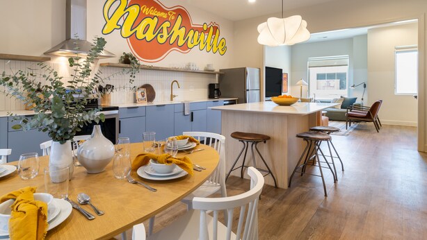 Una cocina moderna con una isla central, muebles blancos y un comedor con mantel amarillo.