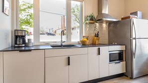 Eine moderne Küche mit einem Edelstahl-Kühlschrank, einem eingebauten Backofen, einer Kaffeemaschine und einem Fenster mit Blick auf die Straße.