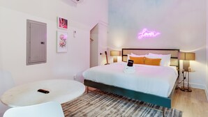 A modern bedroom with a bed, bedside tables, a small round table, and a neon sign on the wall. - Conway | Group Travel | Sleeps 28 in DT (Nashville)