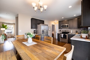 A modern kitchen with dark cabinets, stainless steel appliances, and a wooden dining table. - Two Spacious Living Areas | Modern & Stylish Haven | Silver Maple by AvantStay (Asheville)