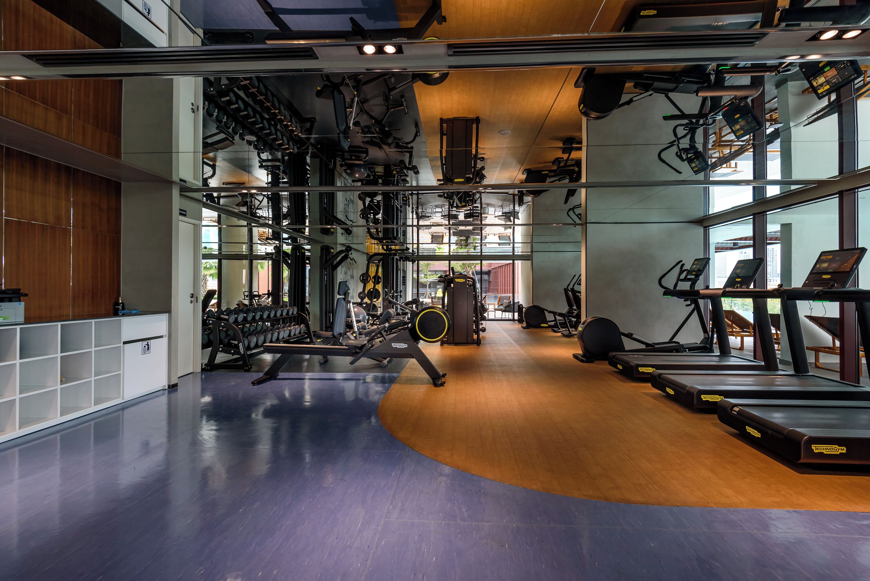 Uma academia moderna com diversos equipamentos de exercício, incluindo esteiras e máquinas de musculação, e piso de madeira.