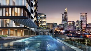 Un hôtel moderne doté d’une piscine à débordement sur le toit, offrant une vue sur les toits de la ville au crépuscule.