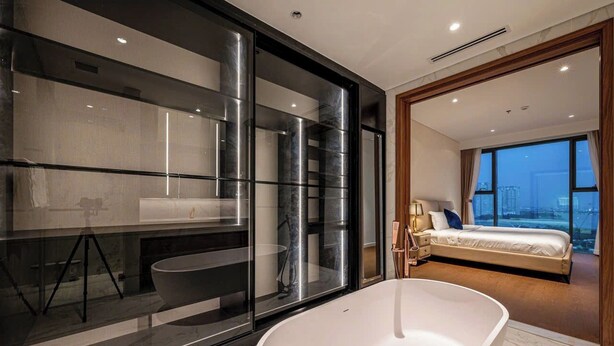Une salle de bain moderne dotée d’une grande baignoire, d’une douche à parois de verre et d’un lit visible dans la pièce adjacente.
