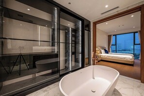 A modern bathroom with a large bathtub, a glass-enclosed shower, and a visible bed in the adjacent room. - The Crest Residence  By An Gia Hospitality (Ho Chi Minh City)