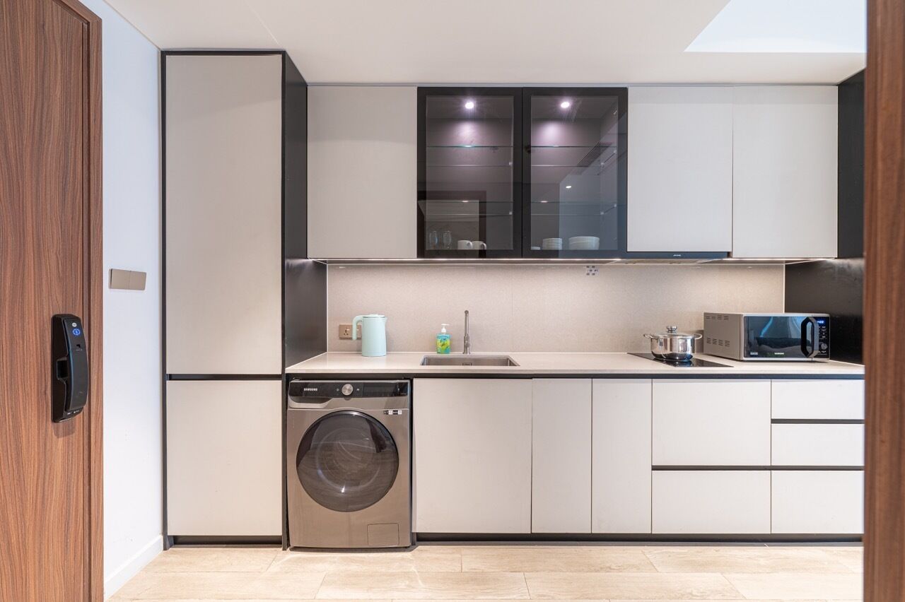 A modern kitchen with a washing machine, microwave, and cabinets.
