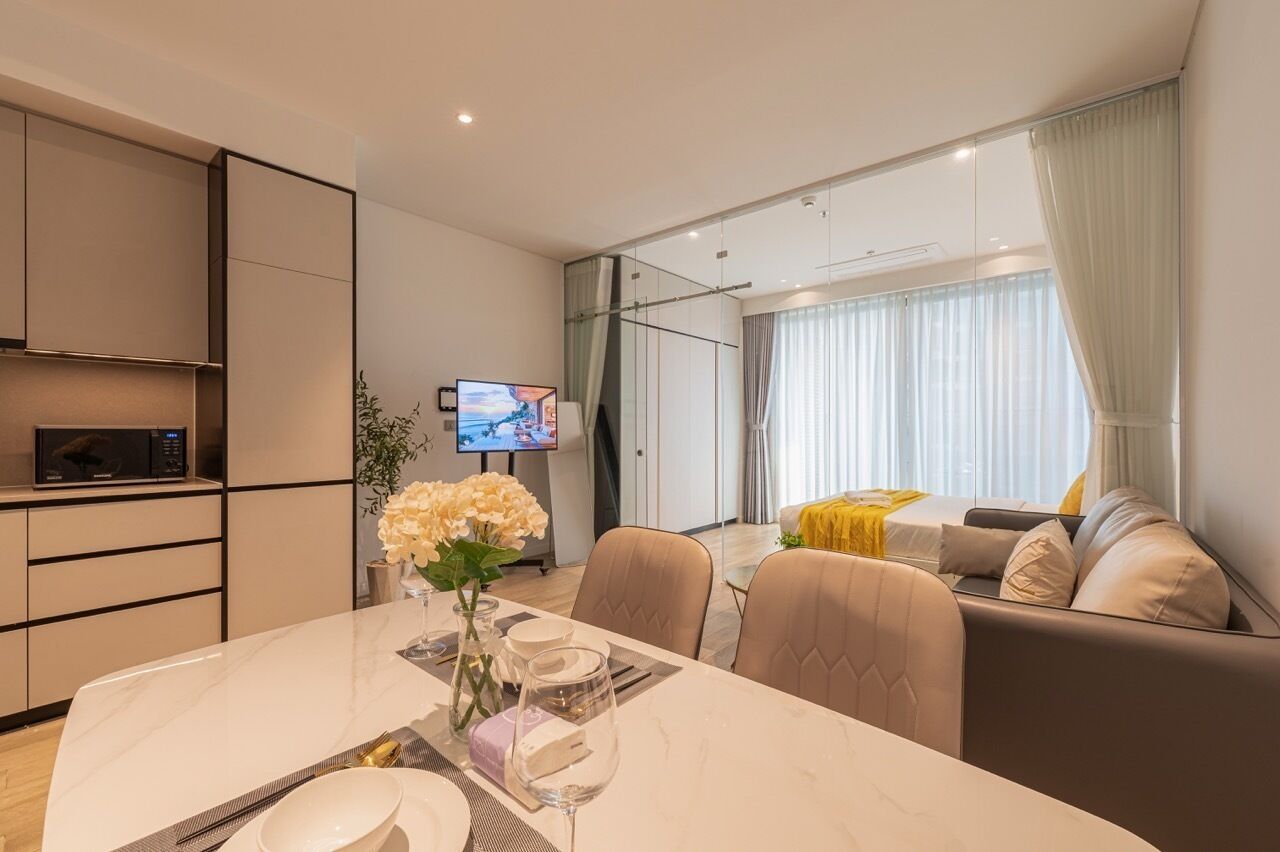Una habitación de hotel moderna con comedor, sofá, televisión y un amplio ventanal con cortinas.