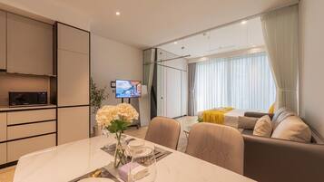 Una habitación de hotel moderna con comedor, sofá, televisión y un amplio ventanal con cortinas.
