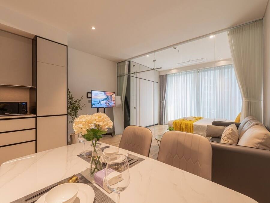 Una habitación de hotel moderna con comedor, sofá, televisión y un amplio ventanal con cortinas.