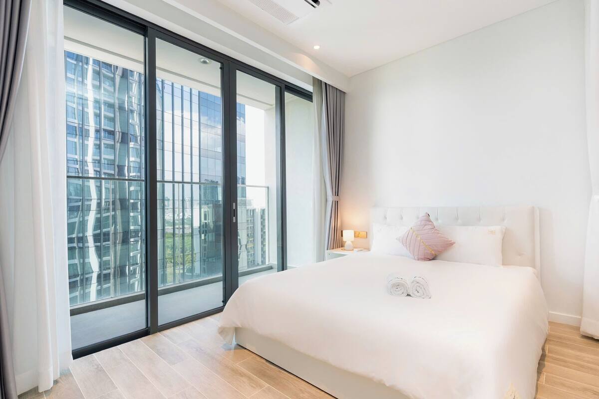 Una habitación de hotel moderna con una cama grande, una mesita de noche, una ventana con cortinas y vistas a la ciudad.