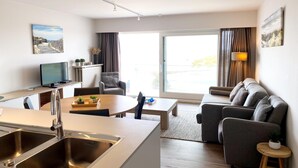 A modern living room with a sofa, a dining table, and a kitchen area with a sink and a television. - Apartment in Nieuwpoort with Sea Views (Nieuwpoort)
