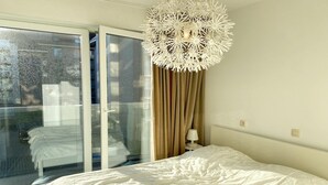 Ein Schlafzimmer mit einem großen Bett, einer weißen Deckenleuchte, einem Fenster mit Vorhängen und Blick nach draußen.