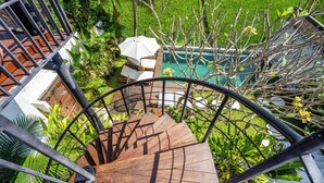 A spiral staircase leading to a pool area surrounded by lush greenery and a white umbrella. - Vista Villa Ubud (Ubud)