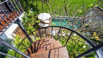 Eine Wendeltreppe führt zu einem Poolbereich, der von üppiger Vegetation und einem weißen Sonnenschirm umgeben ist.