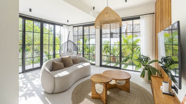 A modern living room with large windows, a sofa, a coffee table, and a hanging light fixture. - Vista Villa Ubud (Ubud)