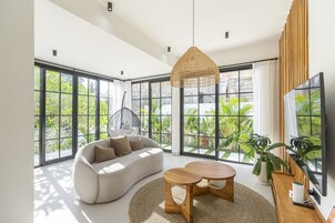 Una sala de estar moderna con ventanas amplias, un sofá, una mesa de centro y una lámpara colgante.