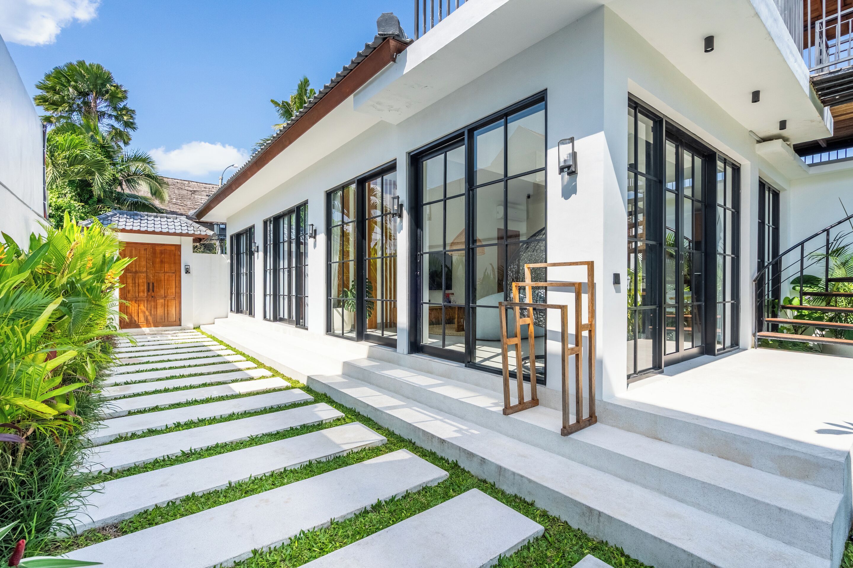 A modern house with a paved pathway leading to the entrance, large windows, and a wooden door.