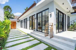 Una casa moderna con un sendero empedrado que lleva a la entrada, ventanas amplias y una puerta de madera.