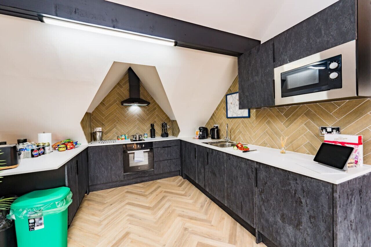 A modern kitchen with dark cabinetry, a herringbone-patterned backsplash, a microwave, and a laptop on the counter.