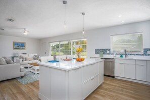 Een moderne keuken met witte kasten, een centraal eiland en een zithoek met een witte bank en salontafel.