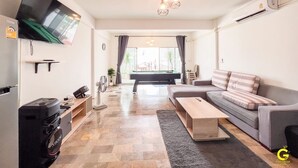 A modern living room with a flat-screen TV, a gaming console, a sofa, a coffee table, and a pool table in the background. - GAO Phala Ocean View Pool Villa (Ban Chang)