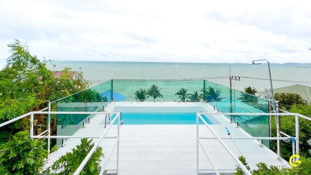 A pool with a glass barrier, surrounded by greenery and overlooking a body of water. - GAO Phala Ocean View Pool Villa (Ban Chang)